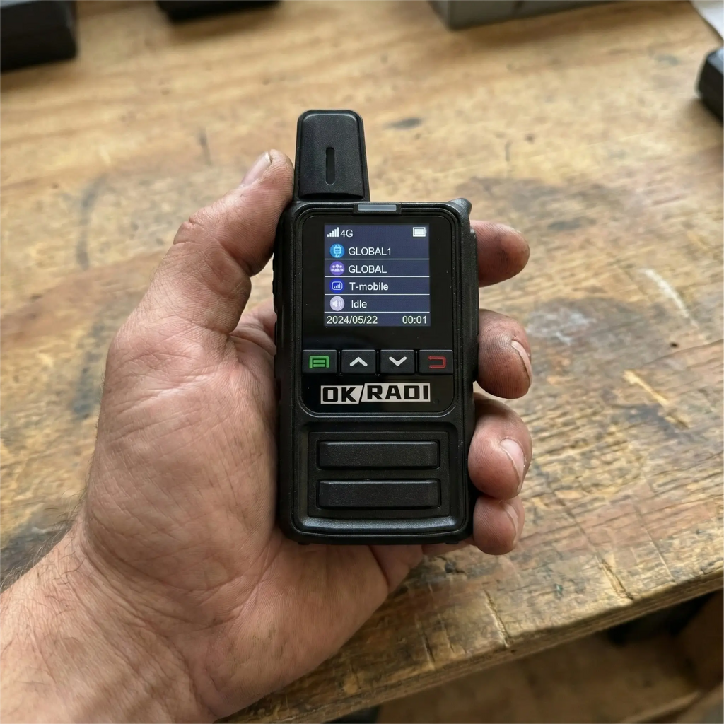 Close up of a hand holding an OKRADI G36 LTE two way radio over a wooden workbench