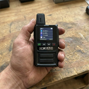 Close up of a hand holding an OKRADI G36 LTE two way radio over a wooden workbench